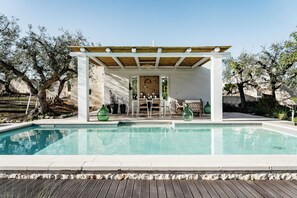 Een zwembad met een pergola, terrasmeubels en een stenen muur op de achtergrond.