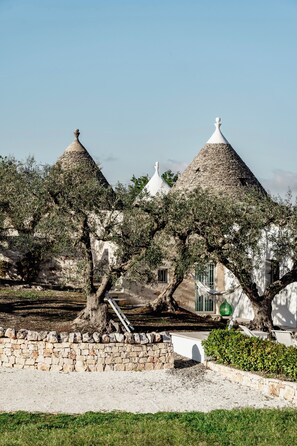 Ein traditionelles Steinhaus mit Kegeldächern, umgeben von Olivenbäumen und einer Steinmauer.