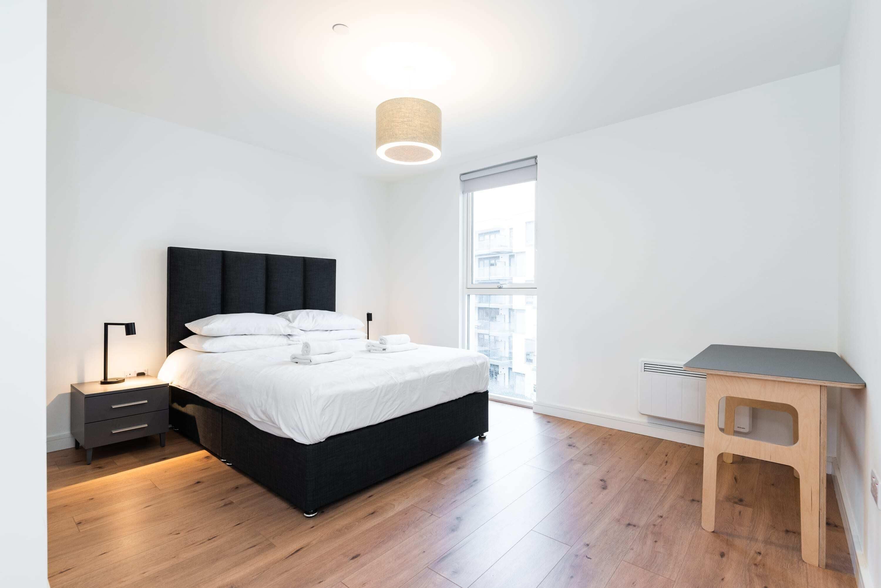 Ein modernes Schlafzimmer mit Bett, Nachttisch, Lampe und einem kleinen Holztisch.