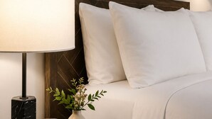 A neatly arranged hotel room with a bed, a bedside table with a lamp, a vase with flowers, and a watch.
