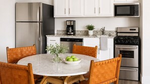 A kitchen with white cabinets, a stainless steel refrigerator, a coffee maker, a microwave, an oven, and a round table with chairs.