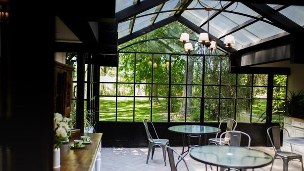 A conservatory with a glass roof, multiple tables, chairs, and a chandelier. - La Matera Posada de Campo (San Rafael)