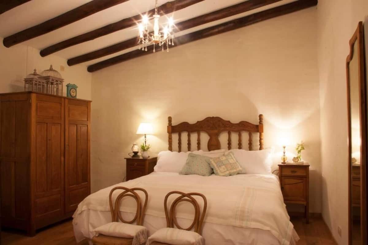 A bedroom with a wooden bed, two bedside tables with lamps, a wooden wardrobe, and a chandelier.
