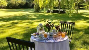 An outdoor dining table set on a grassy lawn with chairs, surrounded by trees.