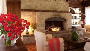 A stone fireplace, a bookshelf, and a vase of red flowers in a cozy room. - La Matera Posada de Campo (San Rafael)