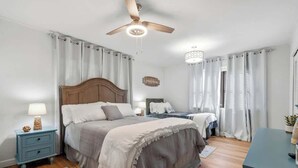 Un dormitorio con cama, mesitas de noche, escritorio, ventilador de techo y candelabro.