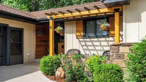 Una casa con porche cubierto, pared de piedra y jardín con diversas plantas y flores.