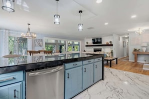 A modern kitchen with a large island, blue cabinets, and a marble floor.
