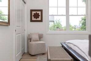 A bedroom with a bed, a chair, a rug, a framed picture, and a window with a view of the outside. - Across From ND Stadium | Luxury 6B/5BA | Sleeps 14 (South Bend)