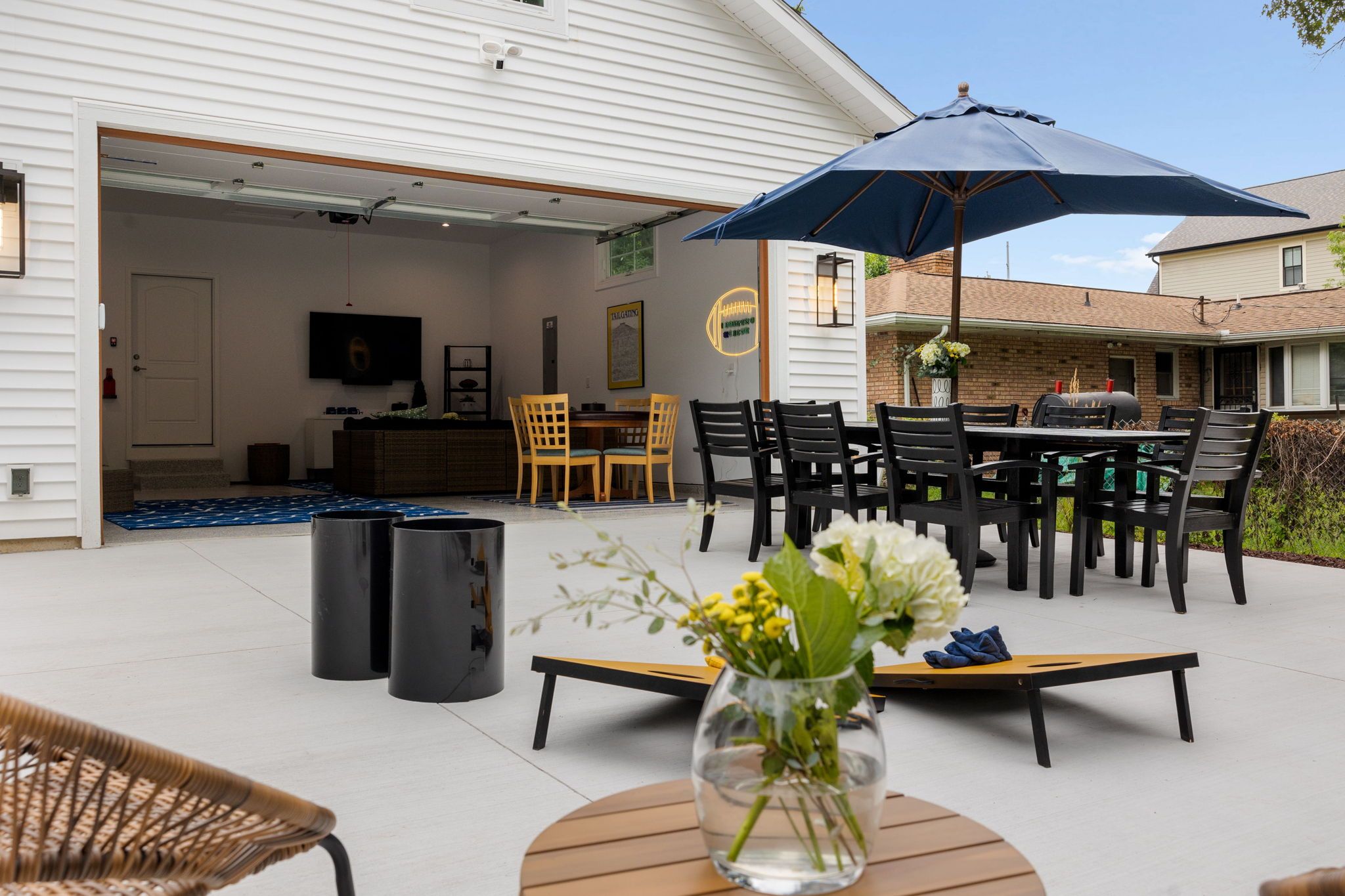 Uma área de terraço ao ar livre com uma mesa de jantar, cadeiras, um grande guarda-sol e um vaso com flores.