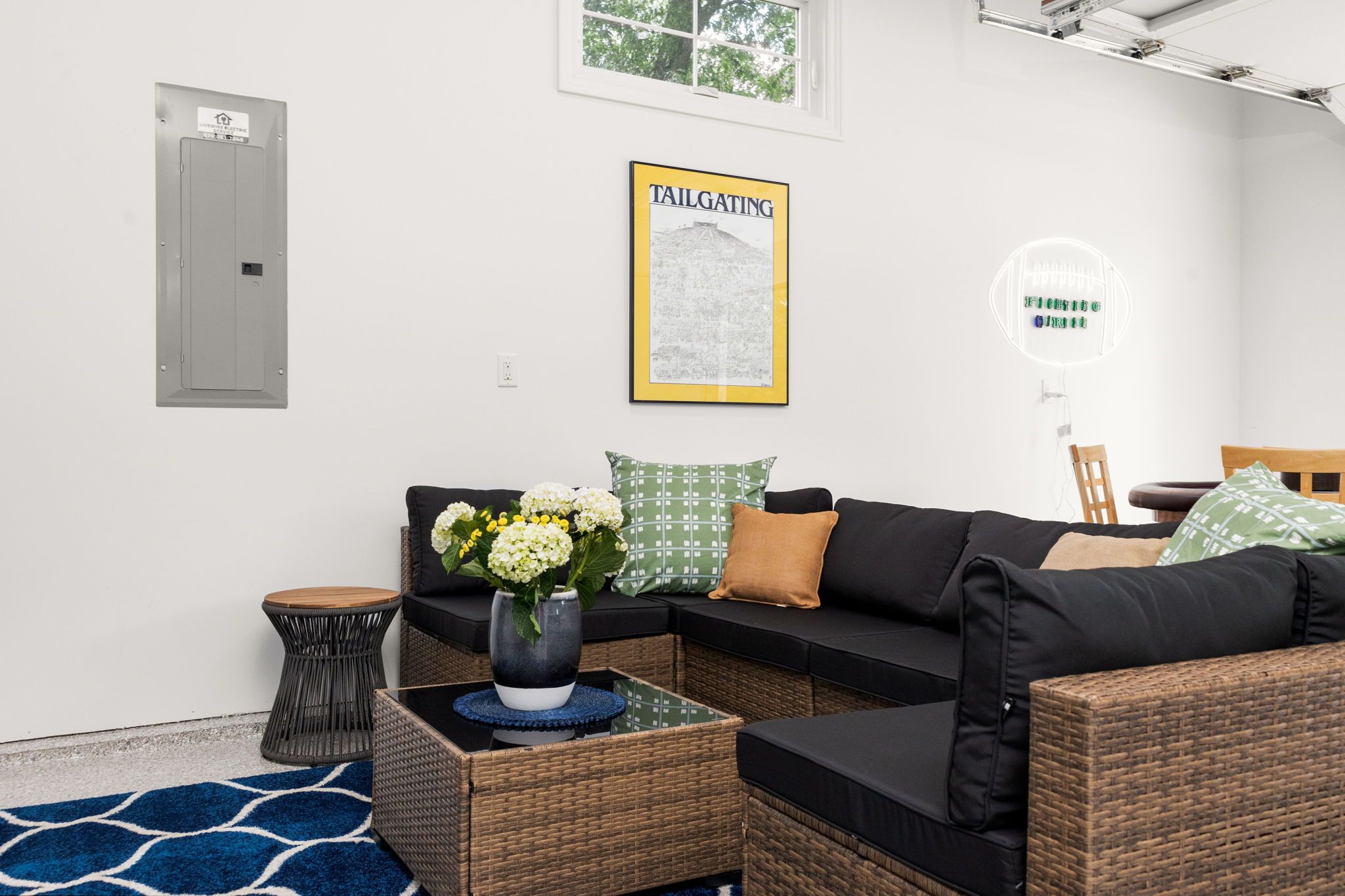 Ein modernes Wohnzimmer mit einem Ecksofa, einem kleinen Beistelltisch, einem Blumenstrauß und einer gerahmten Karte an der Wand.