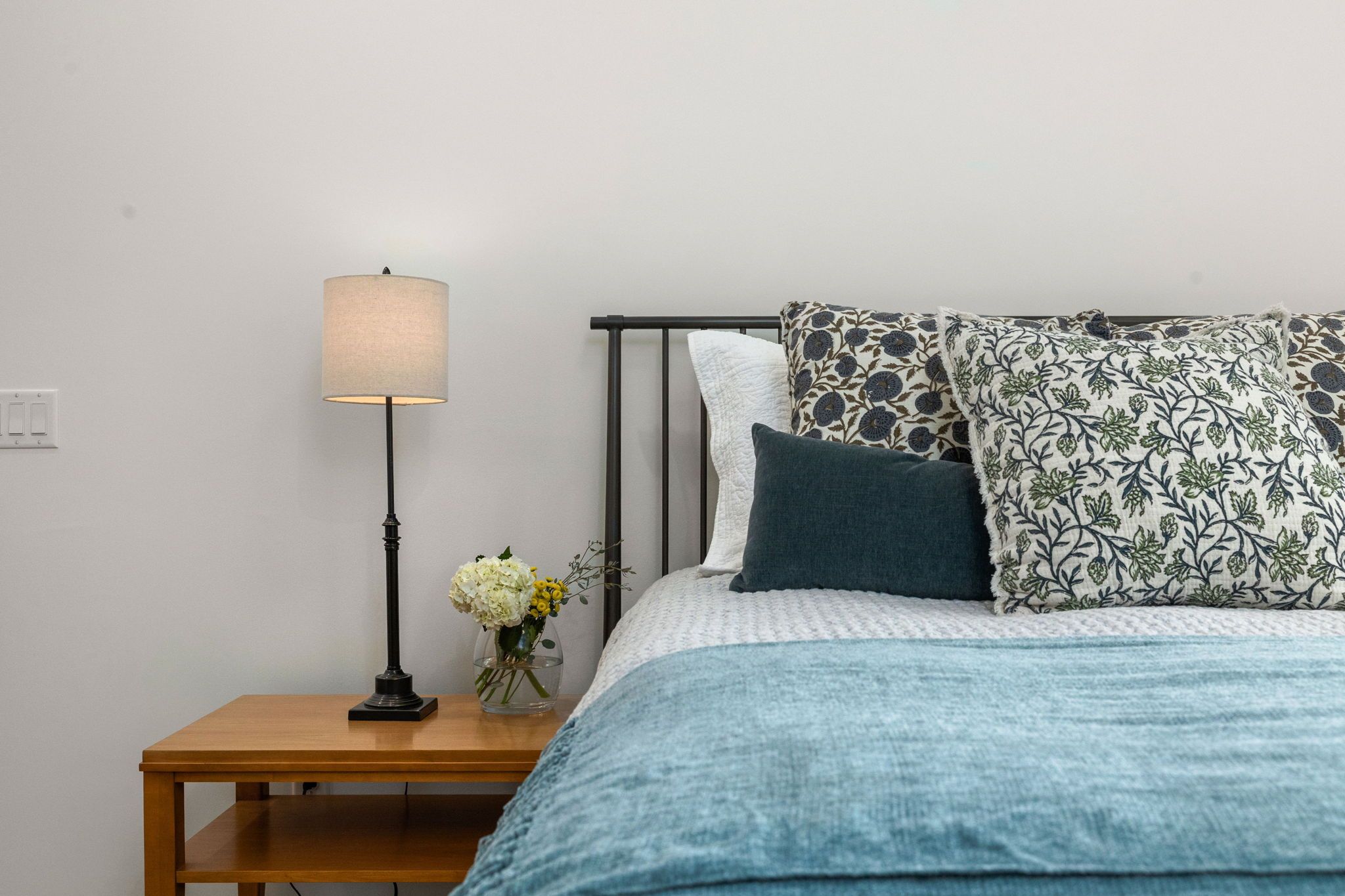 A bedroom with a bed, a nightstand, a lamp, and a vase with flowers.