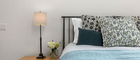 A bedroom with a bed, a nightstand, a lamp, and a vase with flowers.