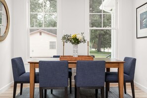 Een eettafel met vier stoelen, een vaas met bloemen en uitzicht op bomen door grote ramen.