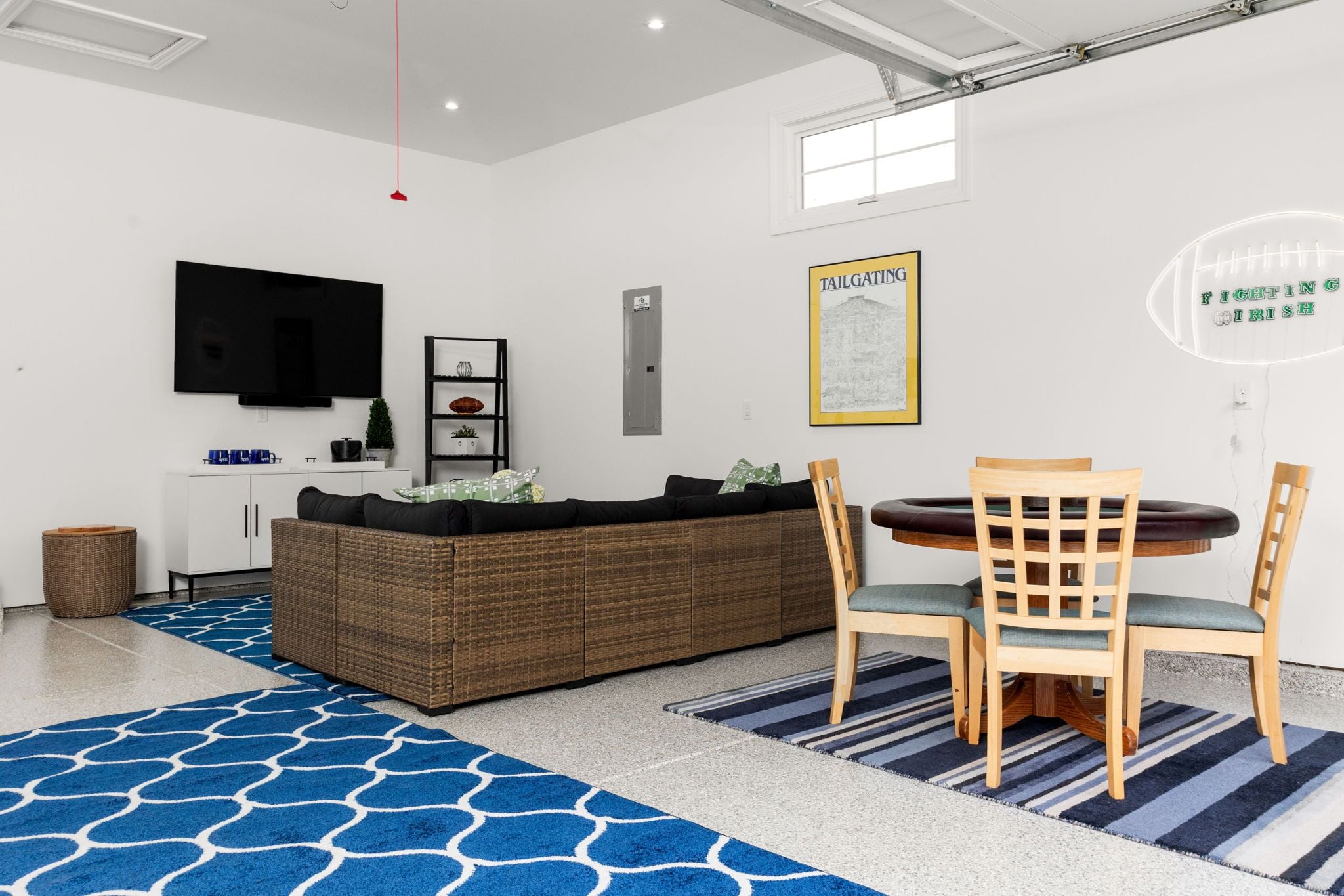 A modern living room with a sofa, a dining table with chairs, a TV mounted on the wall, and a framed picture.
