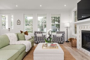A living room with a green sofa, patterned armchairs, a white coffee table, and a fireplace. - Across From ND Stadium | Luxury 6B/5BA | Sleeps 14 (South Bend)
