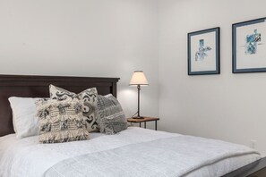 Een net opgemaakt bed met gestreepte kussens, een bedlampje en twee ingelijste kunstwerken aan de muur.