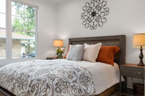 A bedroom with a large bed, two bedside tables, a decorative wall piece, and a window with a view of the outside. - Across From ND Stadium | Luxury 6B/5BA | Sleeps 14 (South Bend)