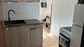 Een kleine keuken met houten kastjes, een zwarte spoelbak, een witte koelkast en een betegelde vloer.