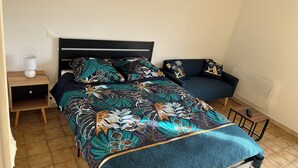 Een bed met een bedspreide, een nachtkastje met een lamp, een donkere bank en een radiator.