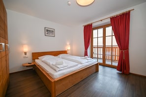 Un dormitorio con una cama de madera, dos mesitas de noche, una lámpara de pared y una ventana con cortinas rojas.