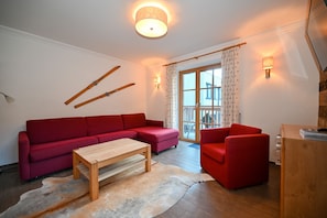 Un sofá rojo, una mesa de centro de madera y un sillón rojo en una sala de estar con piso de madera y un candelabro.