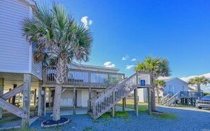 Ein Hotel am Strand mit einer Holzterrasse, Palmen und einer Treppe zum Eingang.