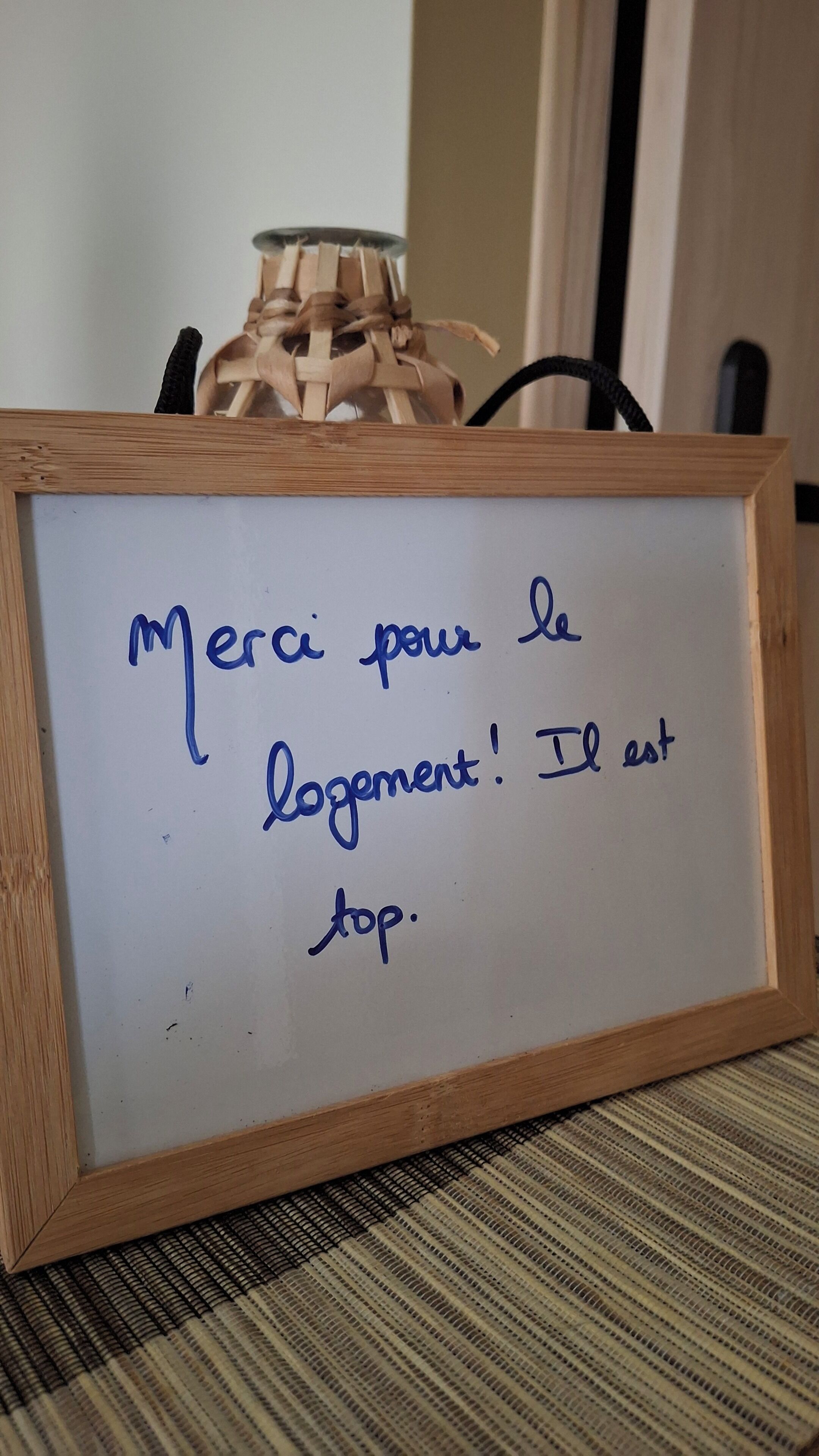 A whiteboard with a message in French, a wooden frame, and a woven basket in the background.