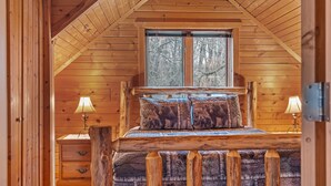 A wooden cabin bedroom with a loft bed, a window with a view of trees, and a nightstand with a lamp. - Rustic Ridge Cabin 102 - Private Woodland Retreat near Devil's Lake State Park (Merrimac)