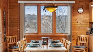 A wooden cabin dining area with a table set for four, a hanging light fixture, and a clock on the wall. - Rustic Ridge Cabin 102 - Private Woodland Retreat near Devil's Lake State Park (Merrimac)