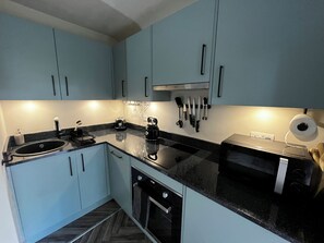 Een moderne keuken met lichtblauwe kastjes, een zwart aanrecht, een waterkoker, een broodrooster, en een set messen die aan de muur hangen.