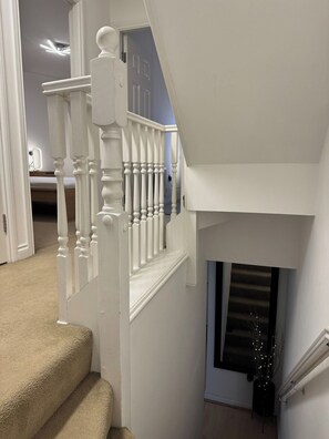 Eine weiße Treppe mit Handlauf, Teppichstufen und einer Tür zu einem anderen Raum.
