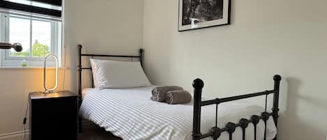 A single bed with a black metal frame, a bedside table with a lamp, and a framed picture on the wall.