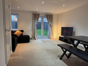 Ein Wohnzimmer mit einer Couch, einem Fernseher, einem Tisch und einer Schiebetür zu einem Garten.