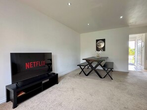 Ein modernes Wohnzimmer mit einem Flachbildfernseher, einem Esstisch und einem gerahmten Bild an der Wand.
