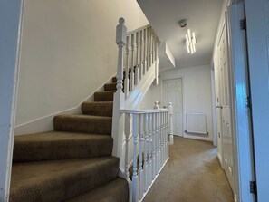 A staircase with carpeted steps and white balusters, leading to a door with a radiator below. - Spacious 4 bed home for Families & contractors. (Sheffield)