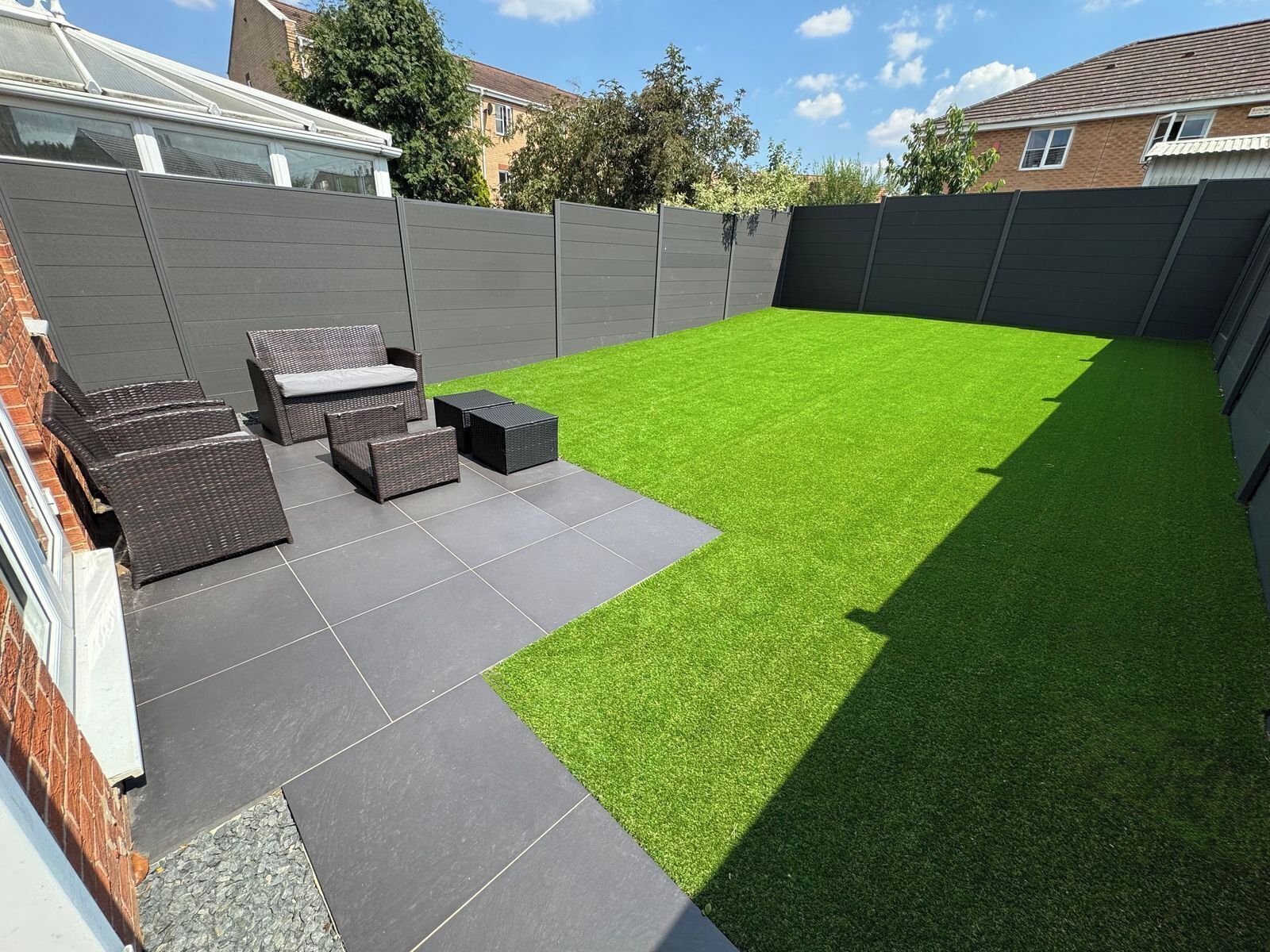 A backyard with artificial grass, a patio area with outdoor furniture, and a grey fence.