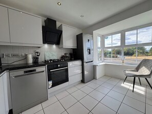 A modern kitchen with white cabinetry, a black stove, and a built-in dishwasher. - Spacious 4 bed home for Families & contractors. (Sheffield)