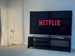 Ein Fernseher mit dem Schriftzug 'NETFLIX' auf dem Bildschirm, ein schwarzer Unterhaltungsschrank und ein Kabelmanagement-System.