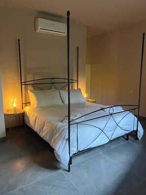 Un letto a baldacchino con biancheria bianca, un comodino con una lampada e un condizionatore d'aria a parete.