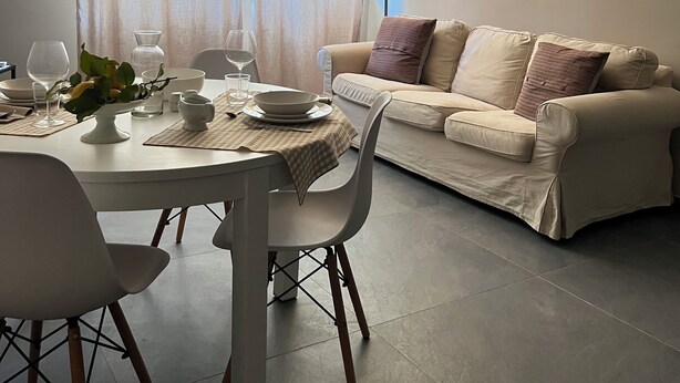 A dining area with a table set for two, a sofa, and a modern lamp.