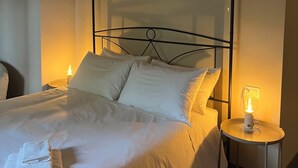 A neatly made bed with white linens and pillows, a bedside table with a lamp, and an air conditioning unit mounted on the wall.