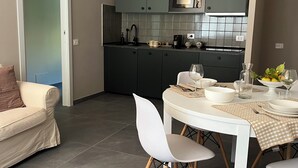 A modern kitchen with dark cabinets, a white dining table with chairs, and a grey tiled floor.
