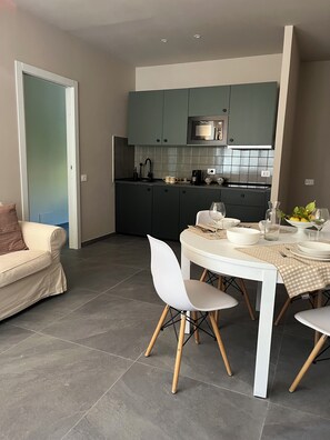 Una cucina moderna con mobili scuri, un tavolo da pranzo bianco con sedie e un pavimento piastrellato grigio.