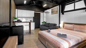 A compact hotel room with a kitchenette, a bed with a patterned bedspread, and a grey sofa. - Modern, exclusive, fully furnished, self-contained 1x1 studio apartment, (Exmouth)