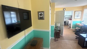A room with a flat-screen TV mounted on the wall, a wooden bench, a door leading to another room, and a tiled floor. - Studio efficiency in the heart of downtown Saint Augustine (St. Augustine)