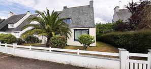 A residential house with a sloped roof, a white fence, and a palm tree. - House with large garden close to beaches. Ideal for families (Saint-Cast-le-Guildo)