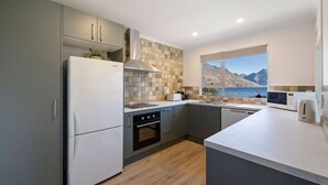 A modern kitchen with a built-in oven, a refrigerator, and a window overlooking a mountainous landscape. - Spectacular Views, Walk To Town, Freshly Renovated (Queenstown)