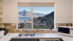 A kitchen with a large window, a sink, a microwave, and a view of mountains and a town. - Spectacular Views, Walk To Town, Freshly Renovated (Queenstown)