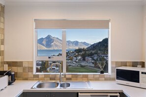 Una cocina con un ventanal grande, un fregadero, un microondas y vistas a montañas y un pueblo.
